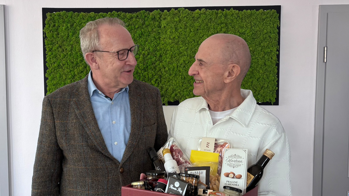 80. jähriger Mitarbeiter mit Geschenbkekorb in der Hand neben Geschäftsführer Harald Ballerstaedt