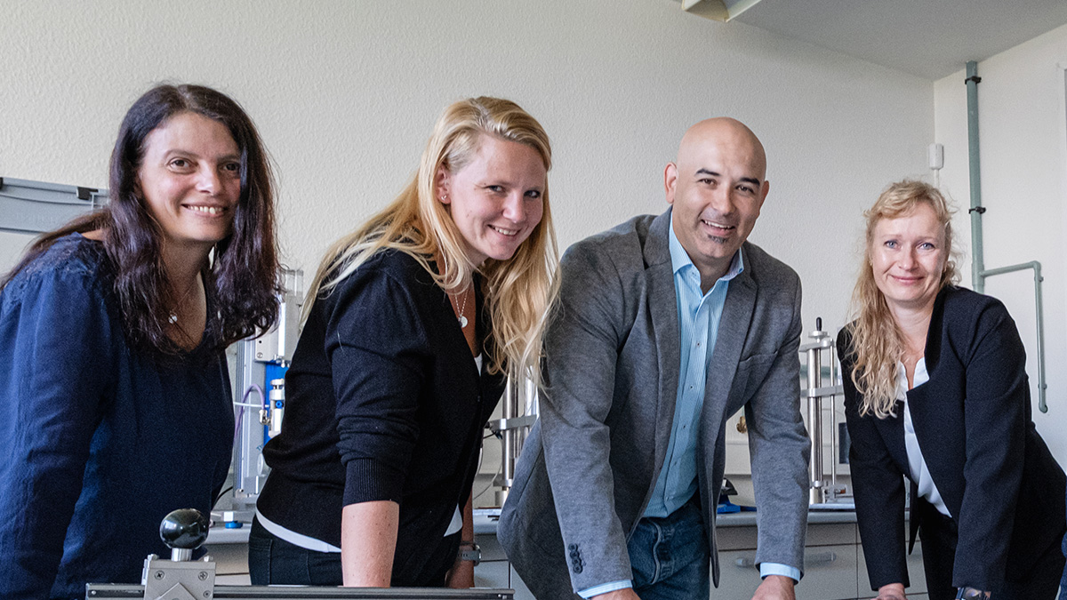 Gruppenbild der Abteilung Qualitätsmanagement und Innovation & Anwendung mit 4 Personen, die sich in einem Labor auf einen Tisch lehnen.