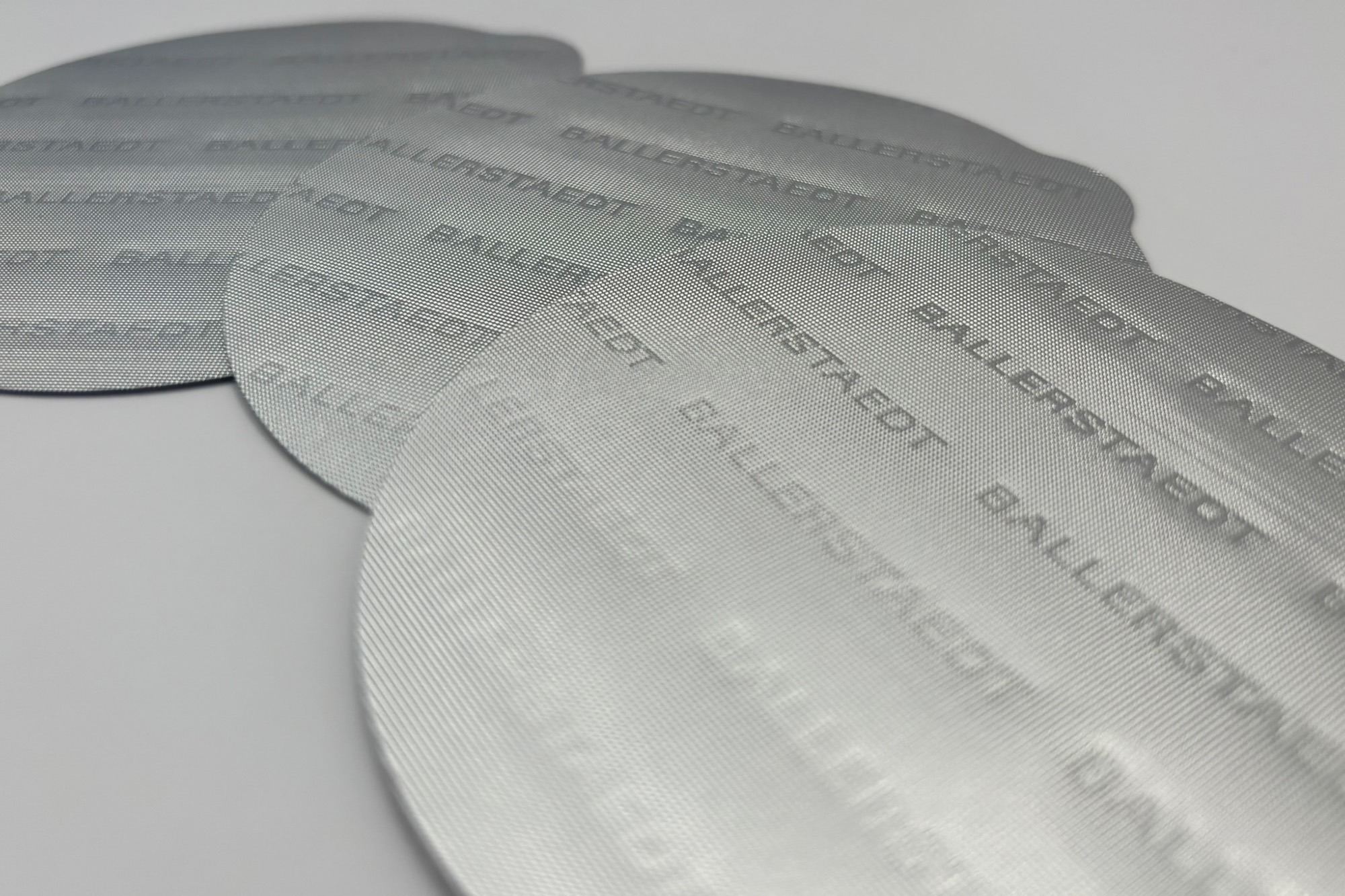 Nahaufnahme einer individuell geprägten Aluminium-Siegelfolie mit BALLERSTAEDT-Logo. Hochwertige Logoprägung für Originalitätsschutz und Markenkommunikation. Nahaufnahme einer individuell geprägten Aluminium-Siegelfolie mit BALLERSTAEDT-Logo. Hochwertige Logoprägung für Originalitätsschutz und Markenkommunikation.